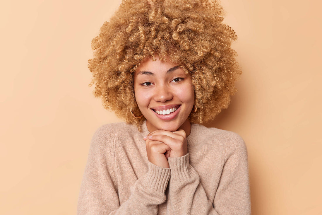Smiling woman with curly hair against a warm peach background.